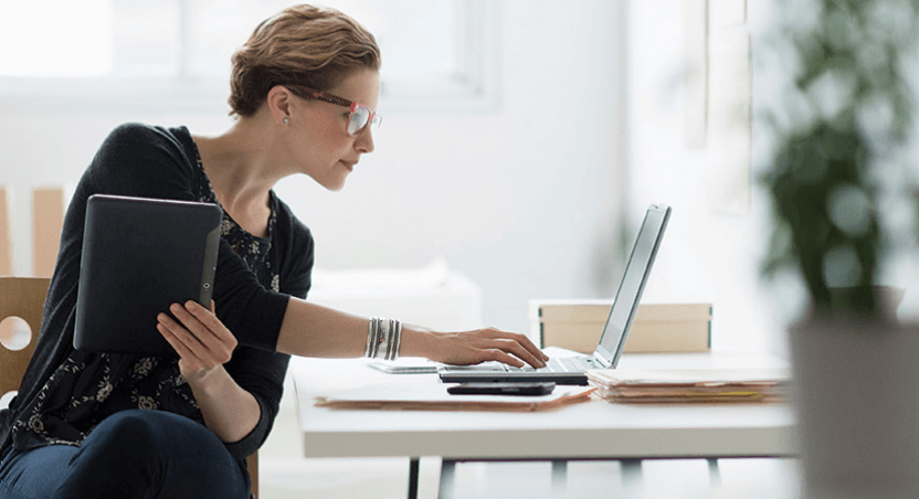 Woman holding a tablet and typing at the notebook